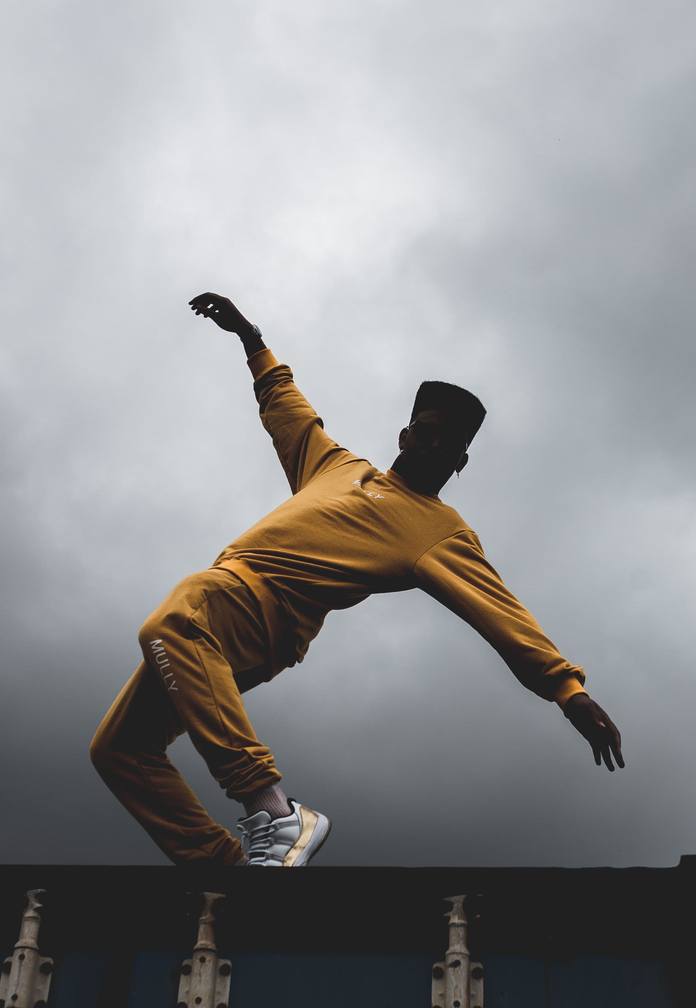 A dancer mid-movement in ochre against an open storm sky — the autumn archive campaign